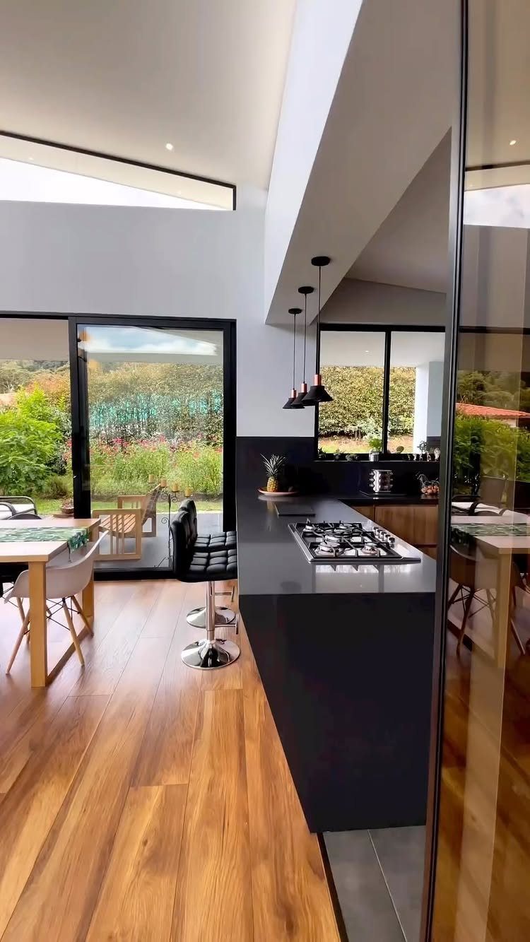 Modern kitchen with a dark island and large windows overlooking a green garden.