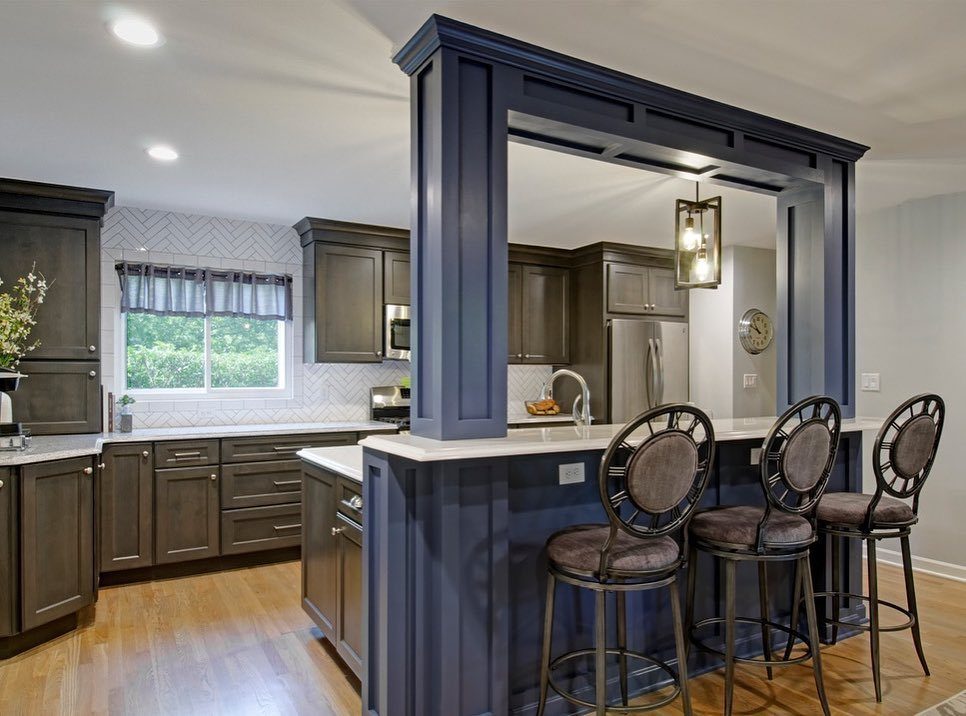 Blue peninsula kitchen counter with three brown bar stools and dark cabinetry.