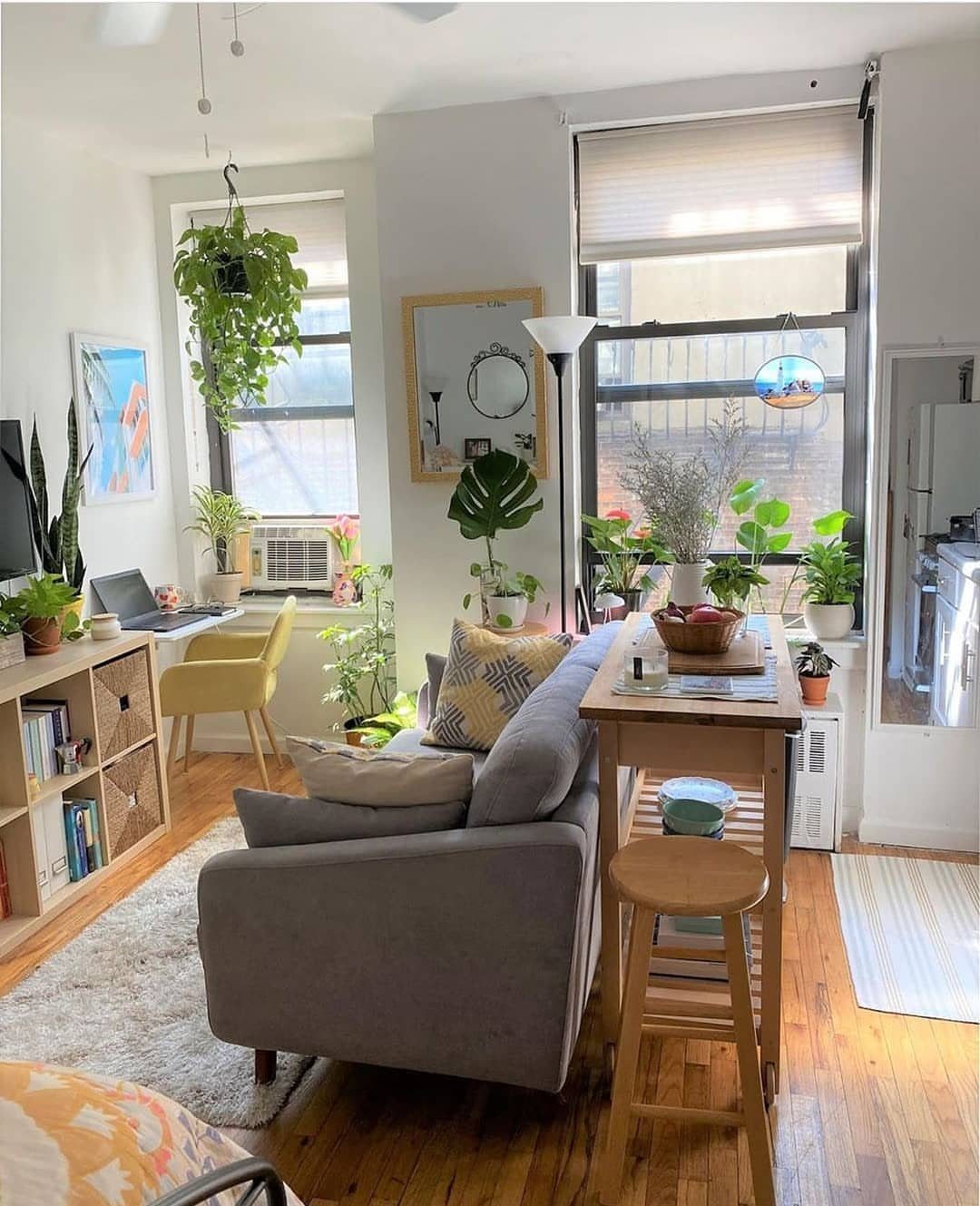 Grey sofa and wooden table with many houseplants in a bright living room.