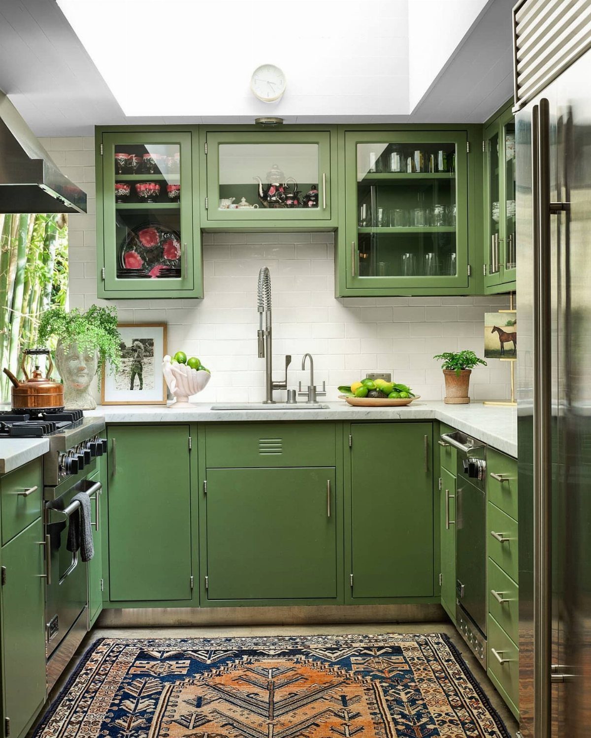 Olive green kitchen cabinets with potted green plants on the white countertop.