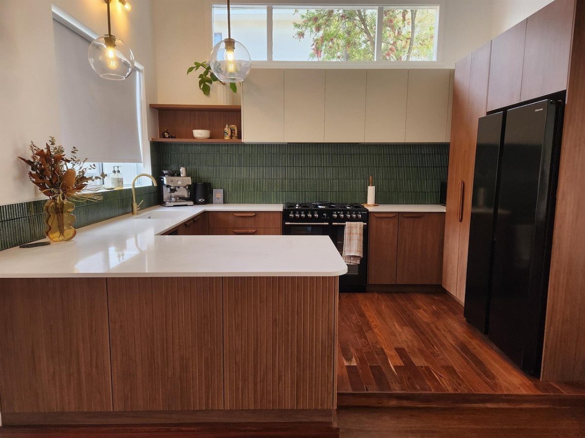 Modern kitchen with wood cabinets, green tile backsplash, and white countertops.