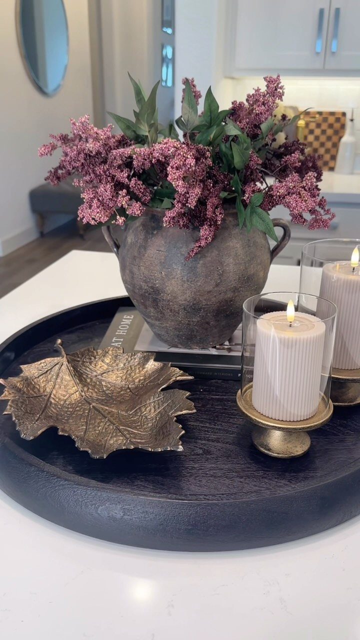 Black tray with purple flowers in a rustic vase and lit white candles.