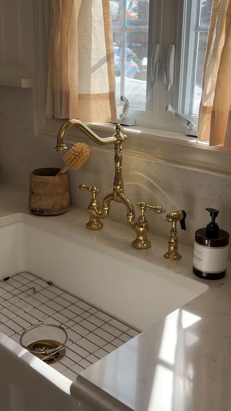 White farmhouse sink with gold faucet, wooden scrub brush, and soap dispenser.