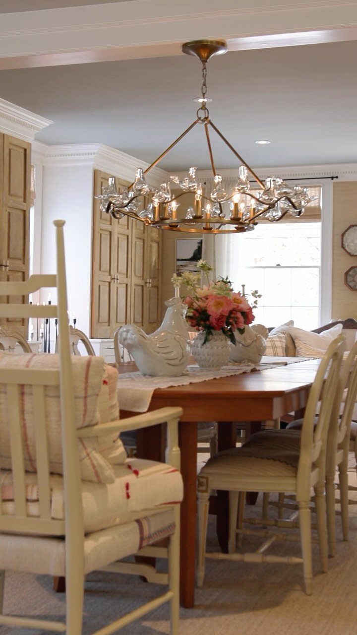 Dining room with cream chairs, wooden table, and a gold chandelier fixture.