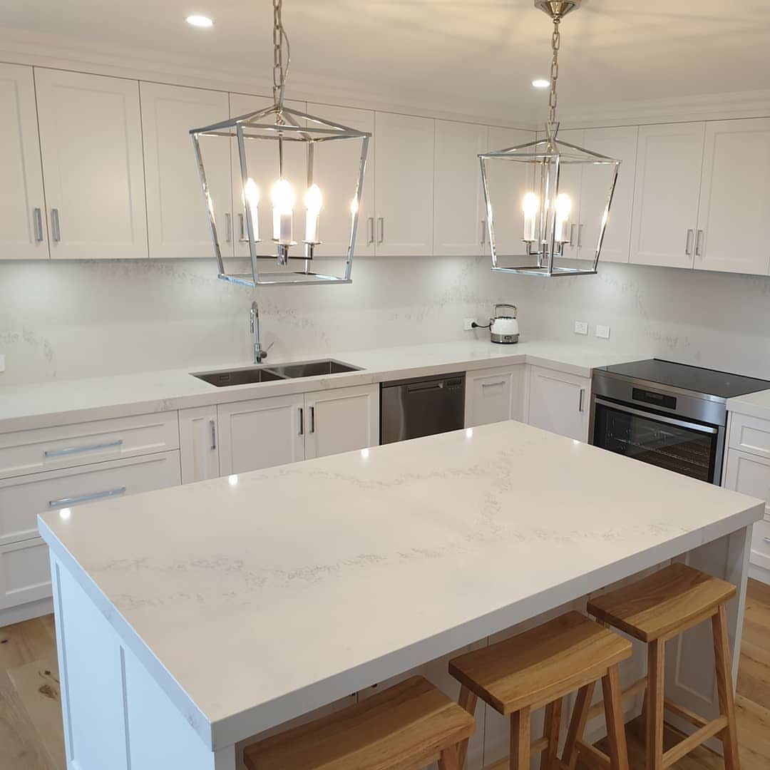 Modern white kitchen with a large island and three wooden bar stools.