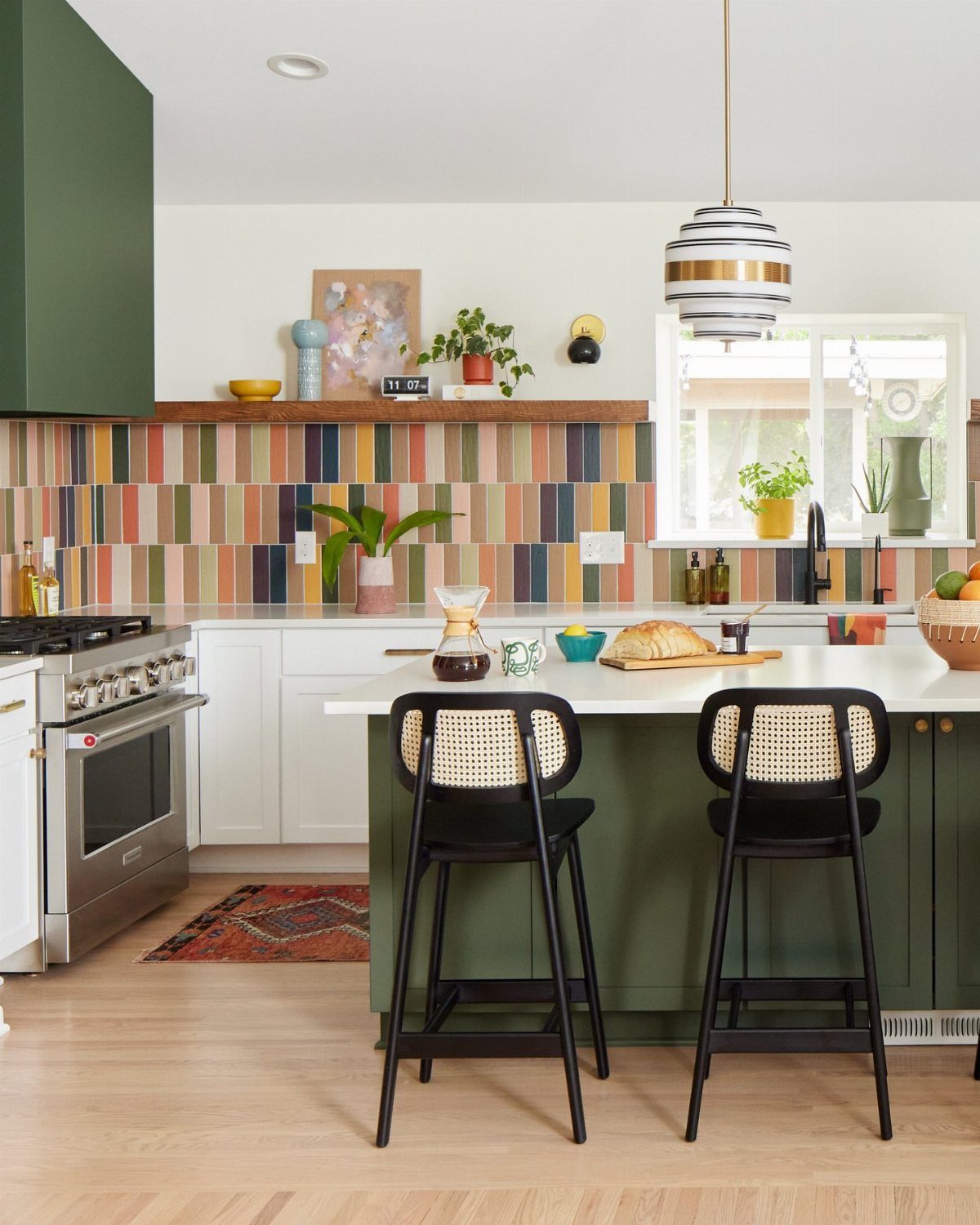 Multi-colored vertical tile backsplash in a modern kitchen with white cabinets and green island.