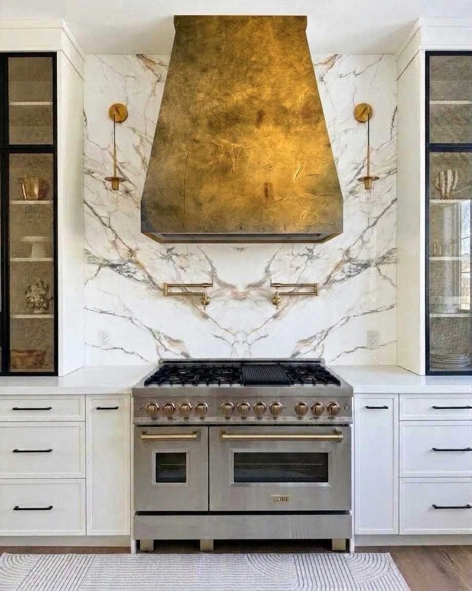 Gold metallic range hood above a stainless steel stove with white marble backsplash