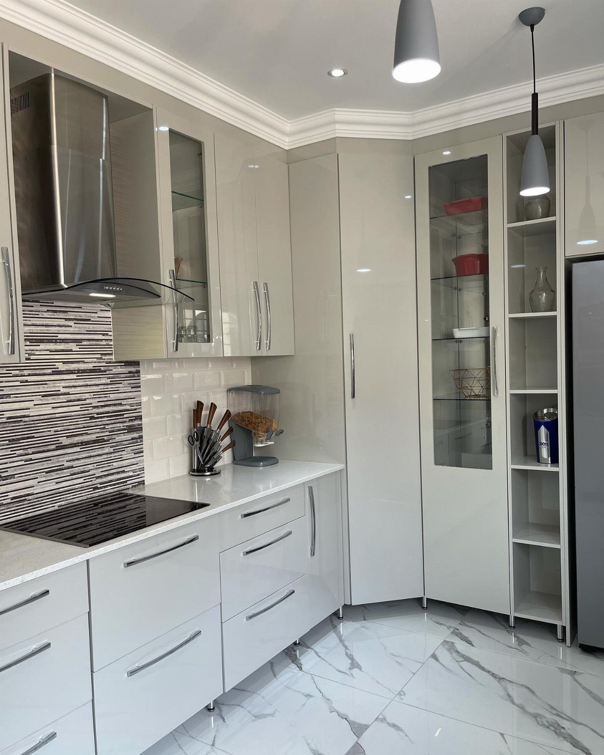 Modern kitchen with glossy white cabinets, marble floors, and linear tiled backsplash.