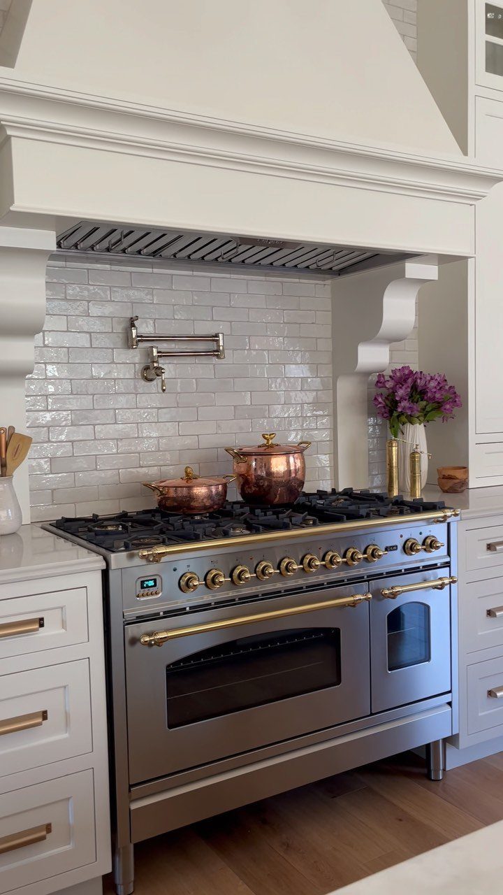 Stainless steel range with gold handles and copper pots in a white kitchen
