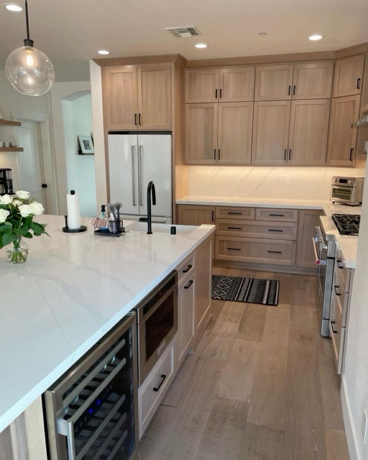 Light wood shaker-style kitchen cabinets with white quartz countertops and stainless steel appliances.