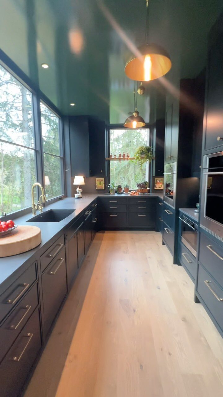 High-gloss moss green kitchen cabinets and ceiling with light wood floors and brass hardware