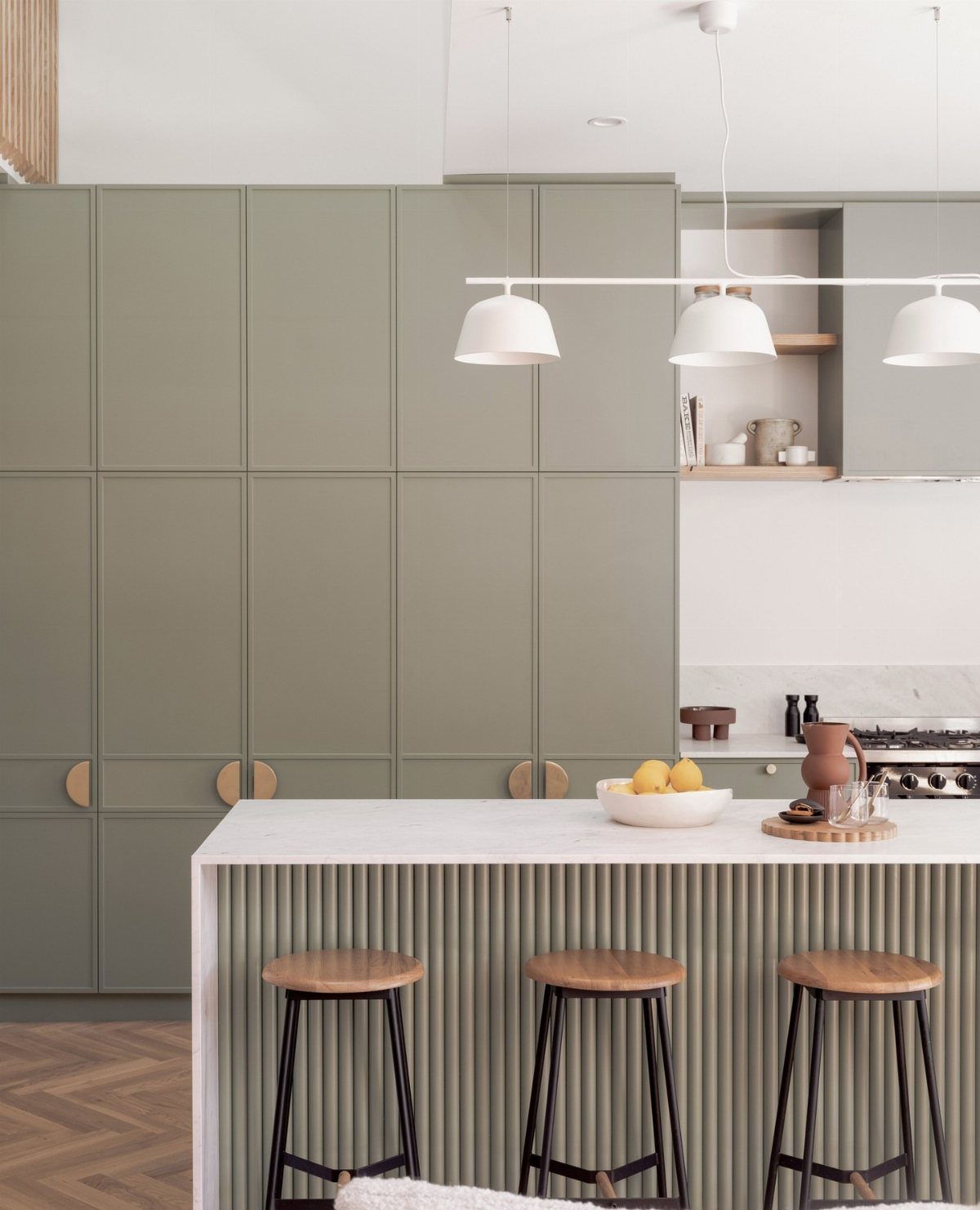 Moss green kitchen cabinets with circular brass handles and a white marble island.