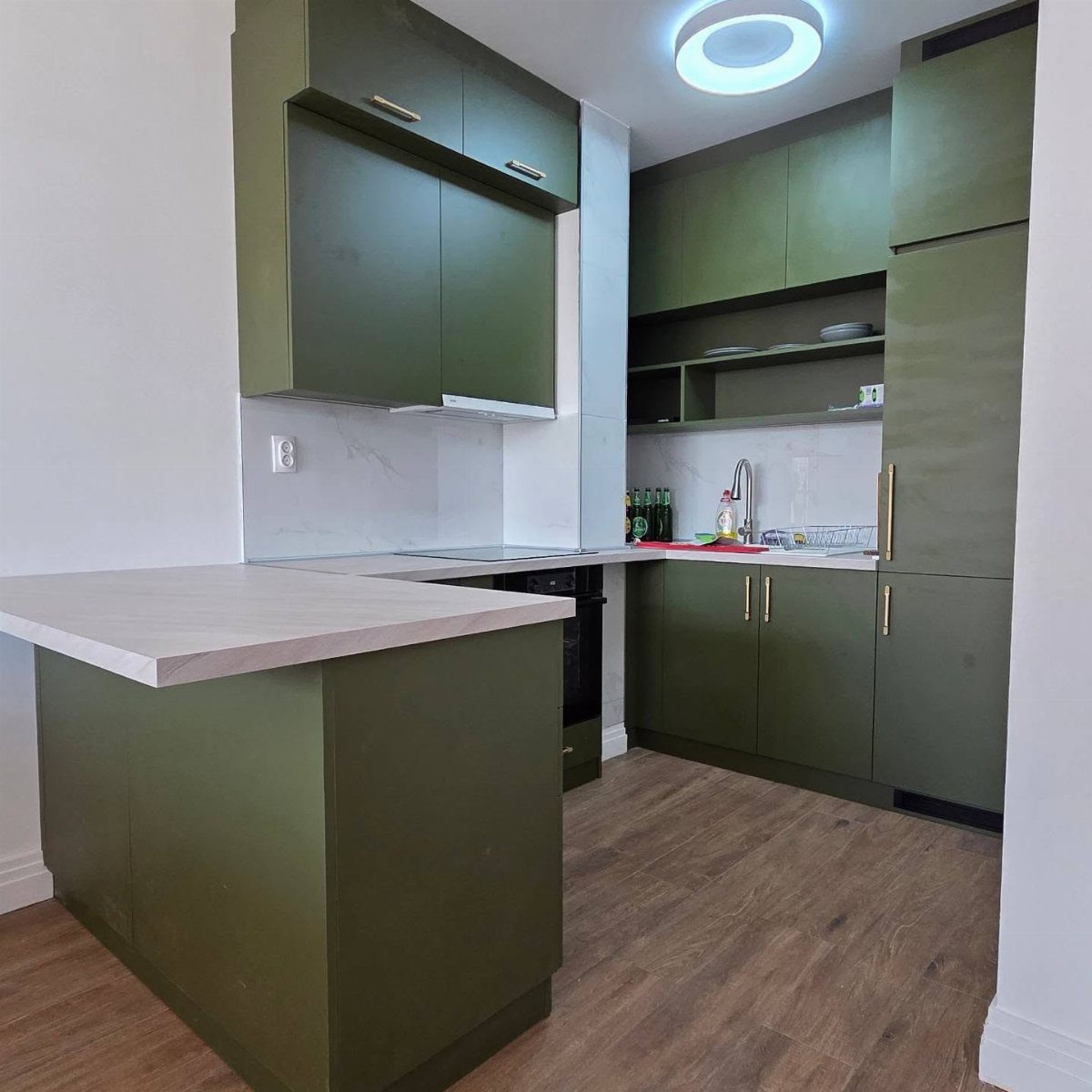 Moss green kitchen cabinets with light countertops and wood-look flooring in a modern room.