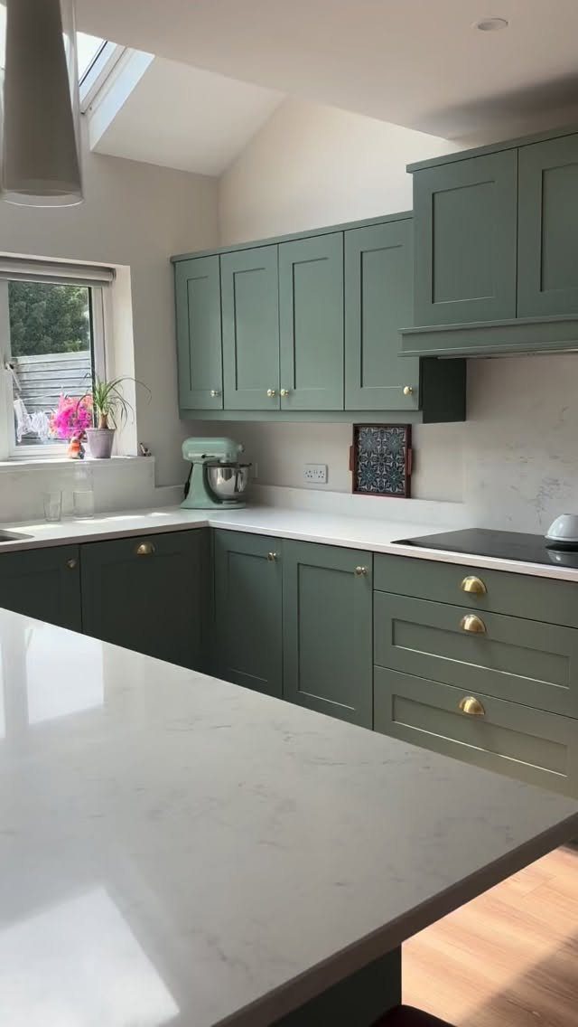 Moss green shaker cabinets with gold hardware and white countertops in a kitchen
