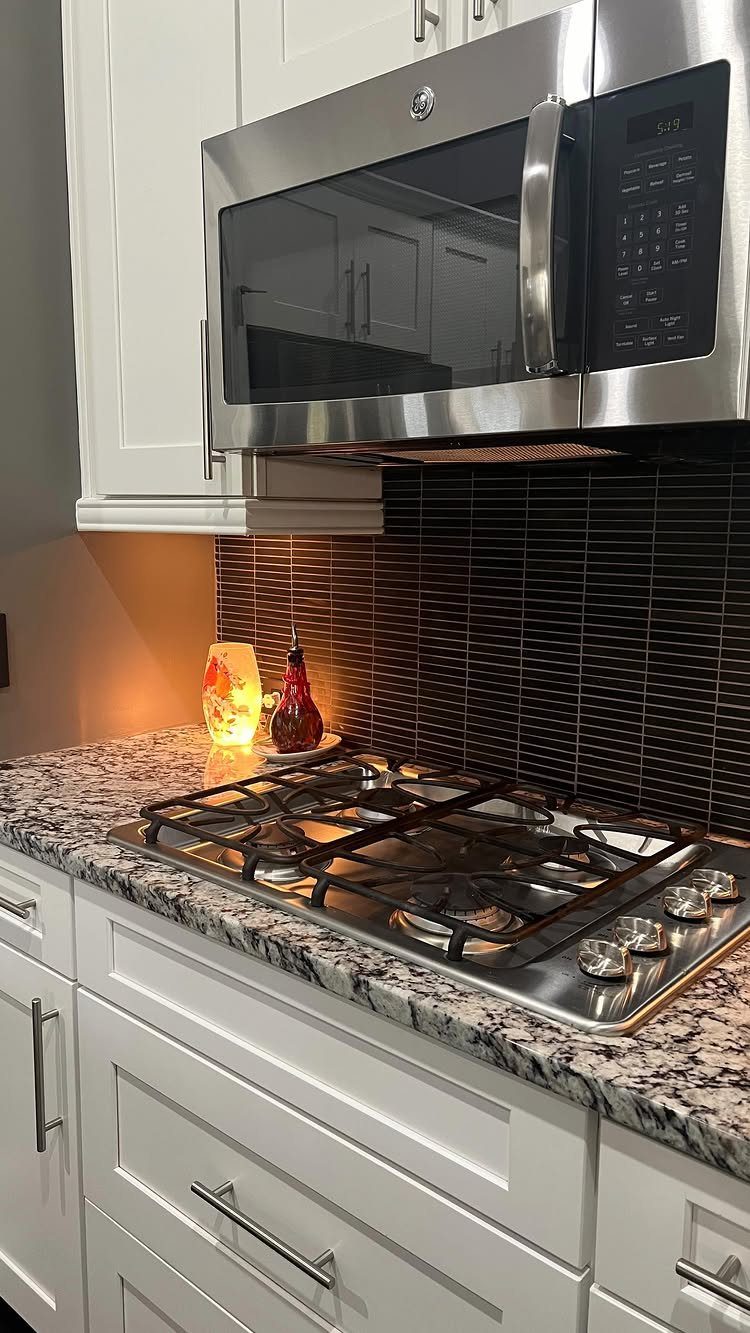 Black basalt subway tile backsplash behind a gas stovetop and stainless steel microwave.