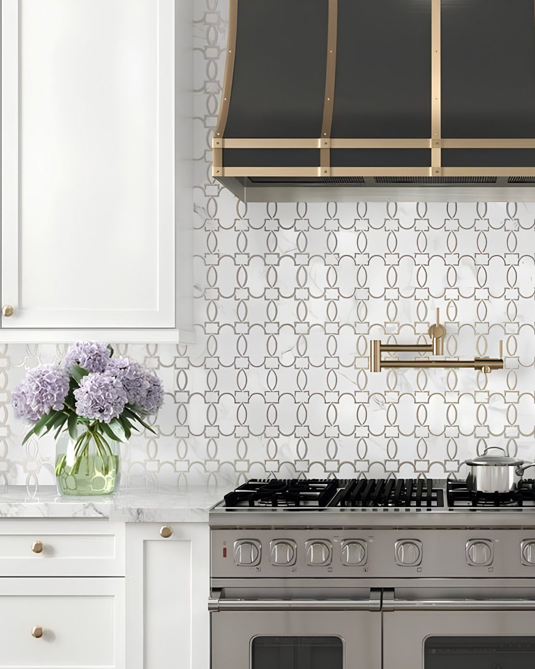 Geometric stone mosaic backsplash in a kitchen with white cabinets and stainless range.