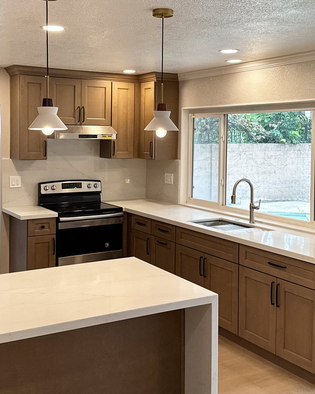 Light brown wood kitchen cabinets with white countertops and pendant lighting.
