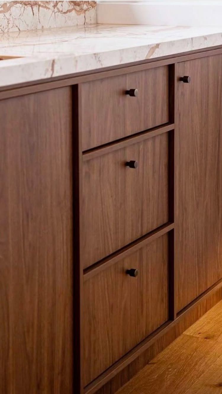 Medium-brown natural wood kitchen cabinets with black knobs and white marble countertops.