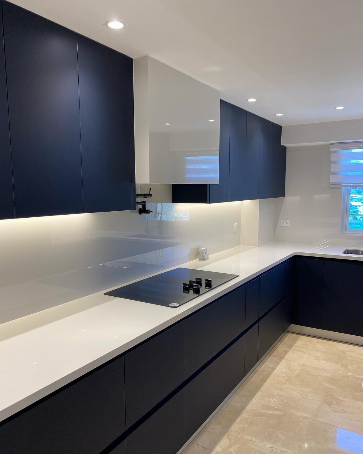 Navy blue kitchen cabinets with white countertops and a sleek white backsplash.