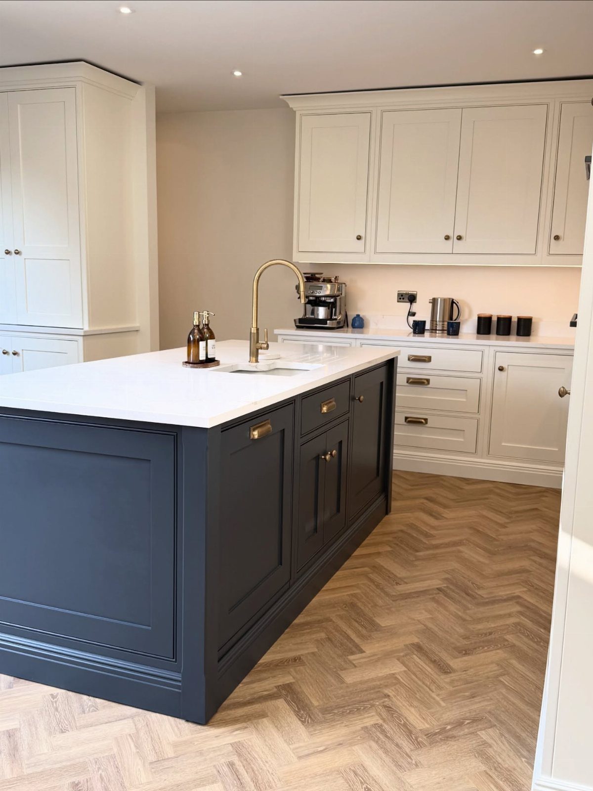 Navy blue kitchen island with cream perimeter cabinets and light wood herringbone floors.