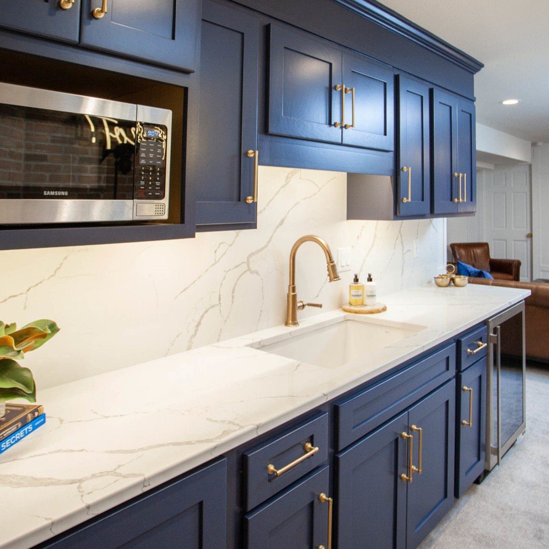 Navy blue kitchen cabinets with brass hardware and white marble countertops and backsplash.