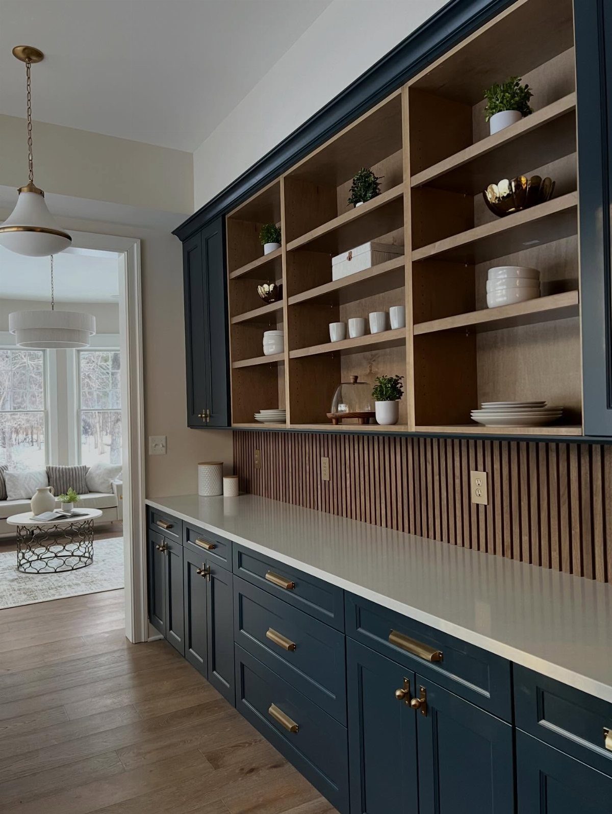 Navy blue kitchen cabinets with gold minimalist pulls and open wooden shelving above.
