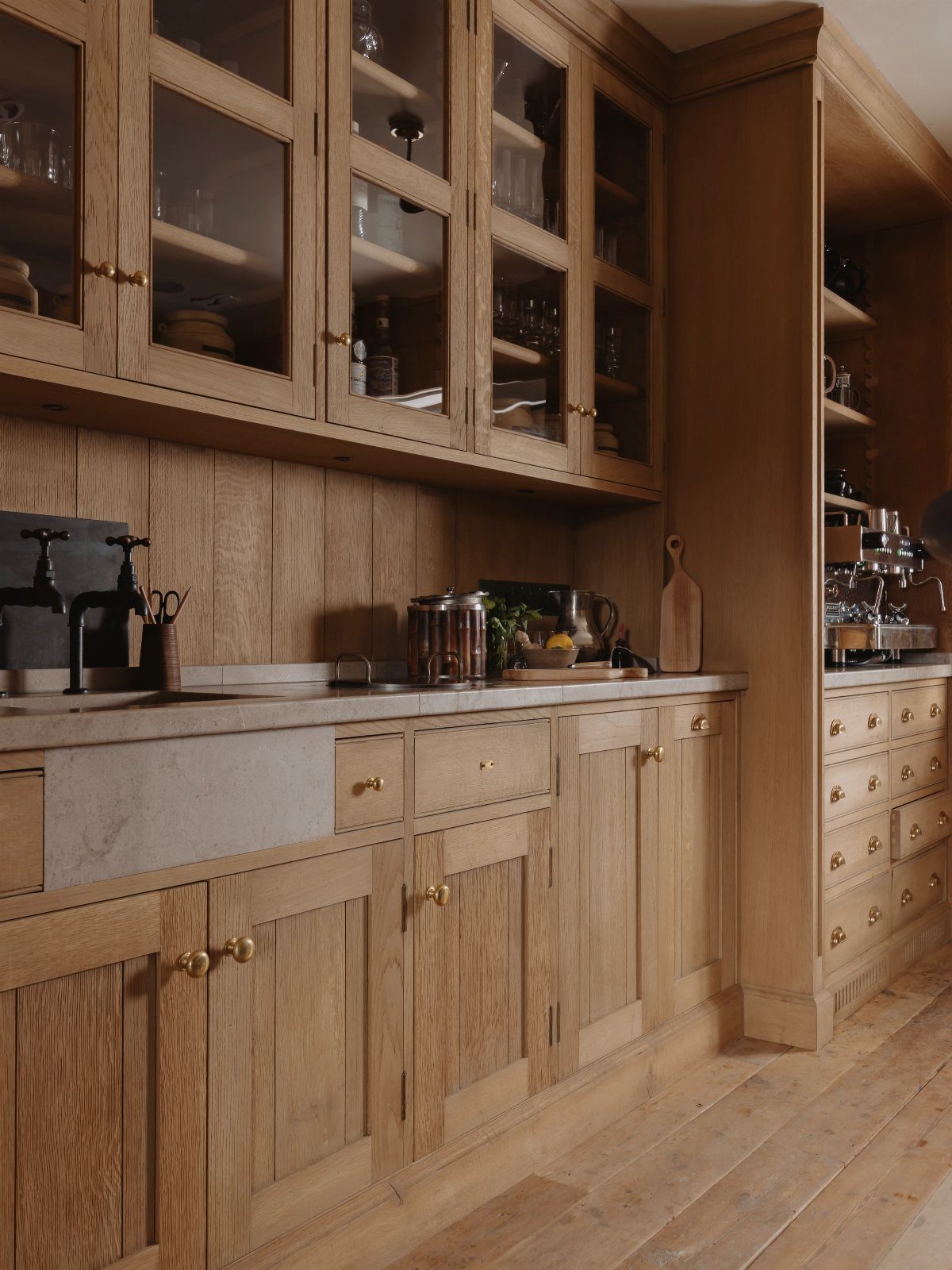 Natural oak kitchen cabinets with glass-front upper doors and a stone farmhouse sink.