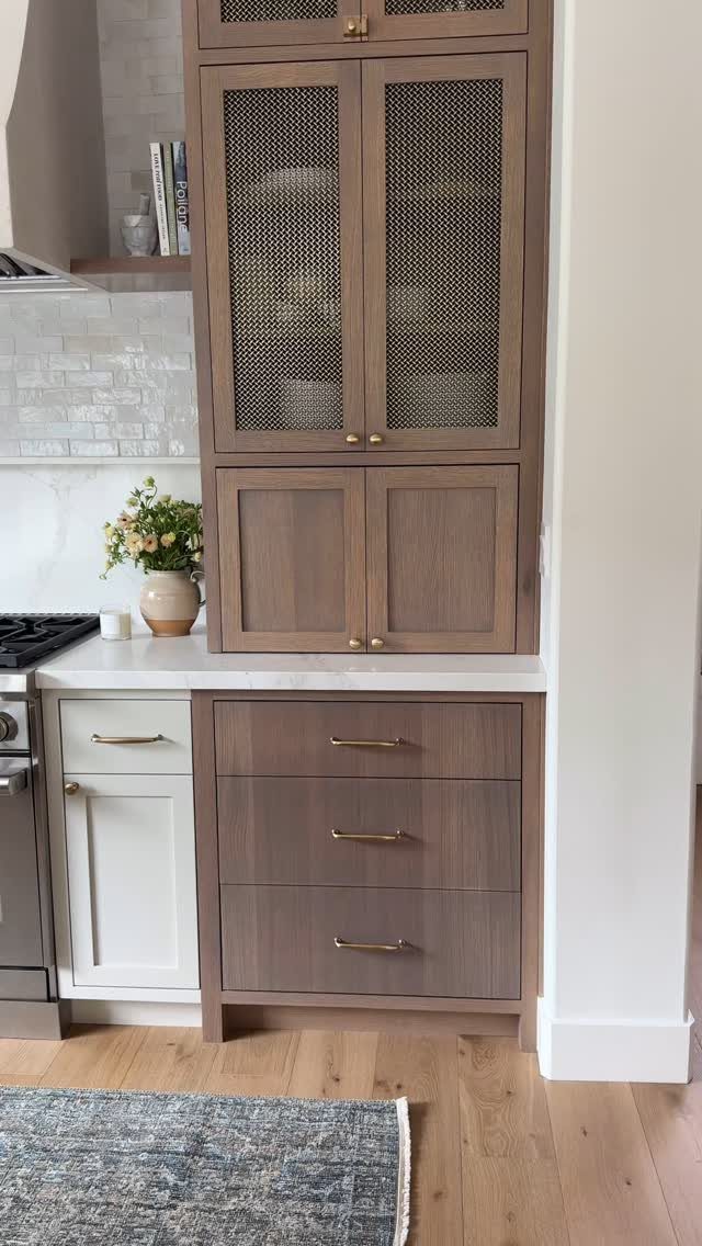 Brown oak kitchen cabinets with mesh doors and gold hardware in a modern kitchen.