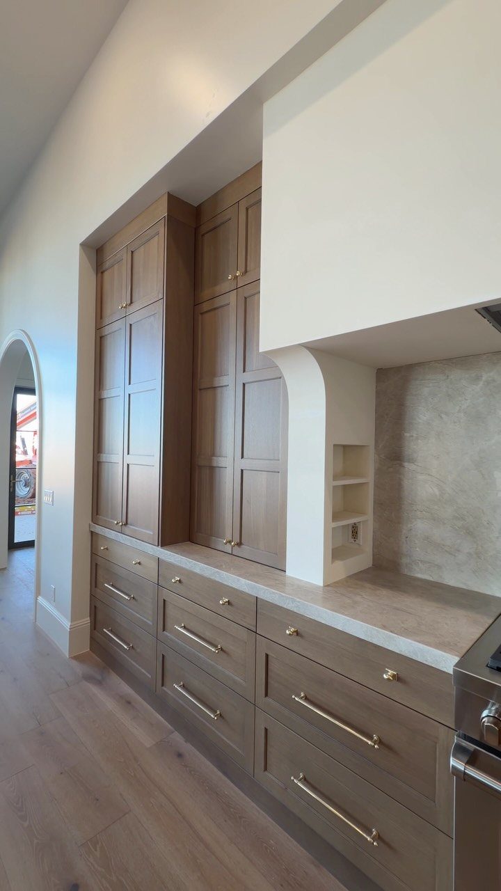 Light-brown stained oak kitchen cabinets with gold handles and matching wood floors.