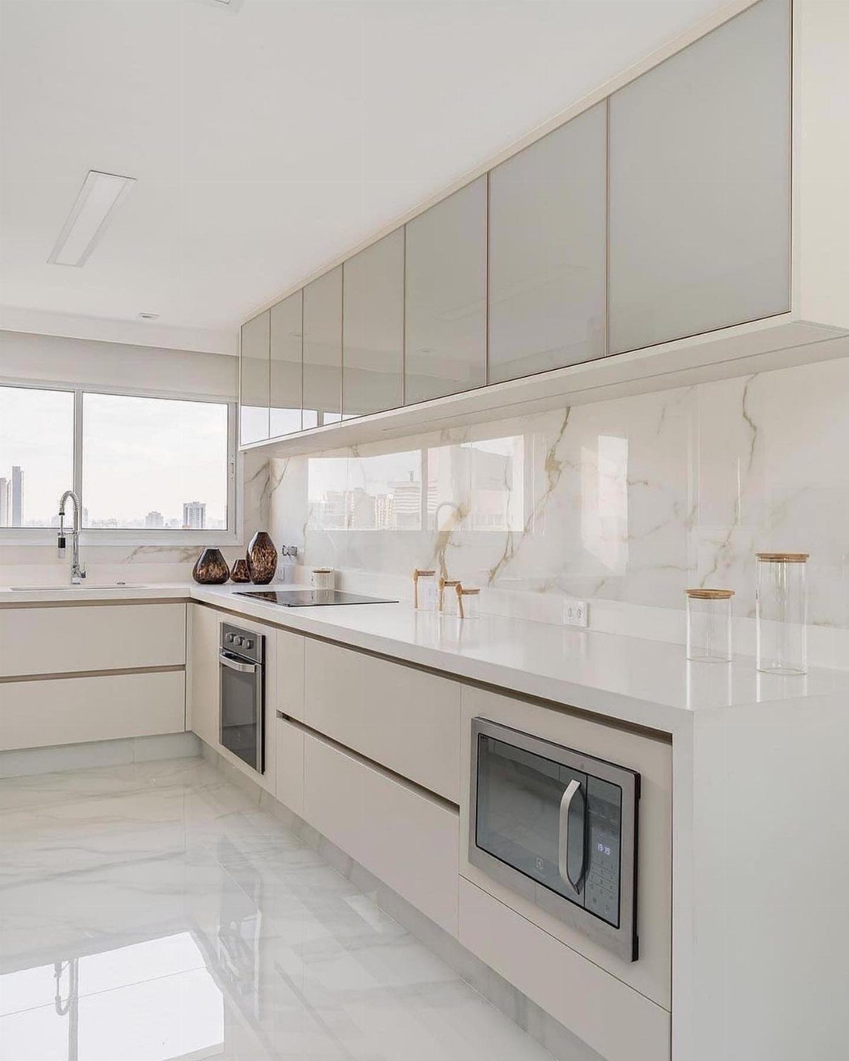 Off-white kitchen cabinets with white marble countertops and matching polished marble flooring.