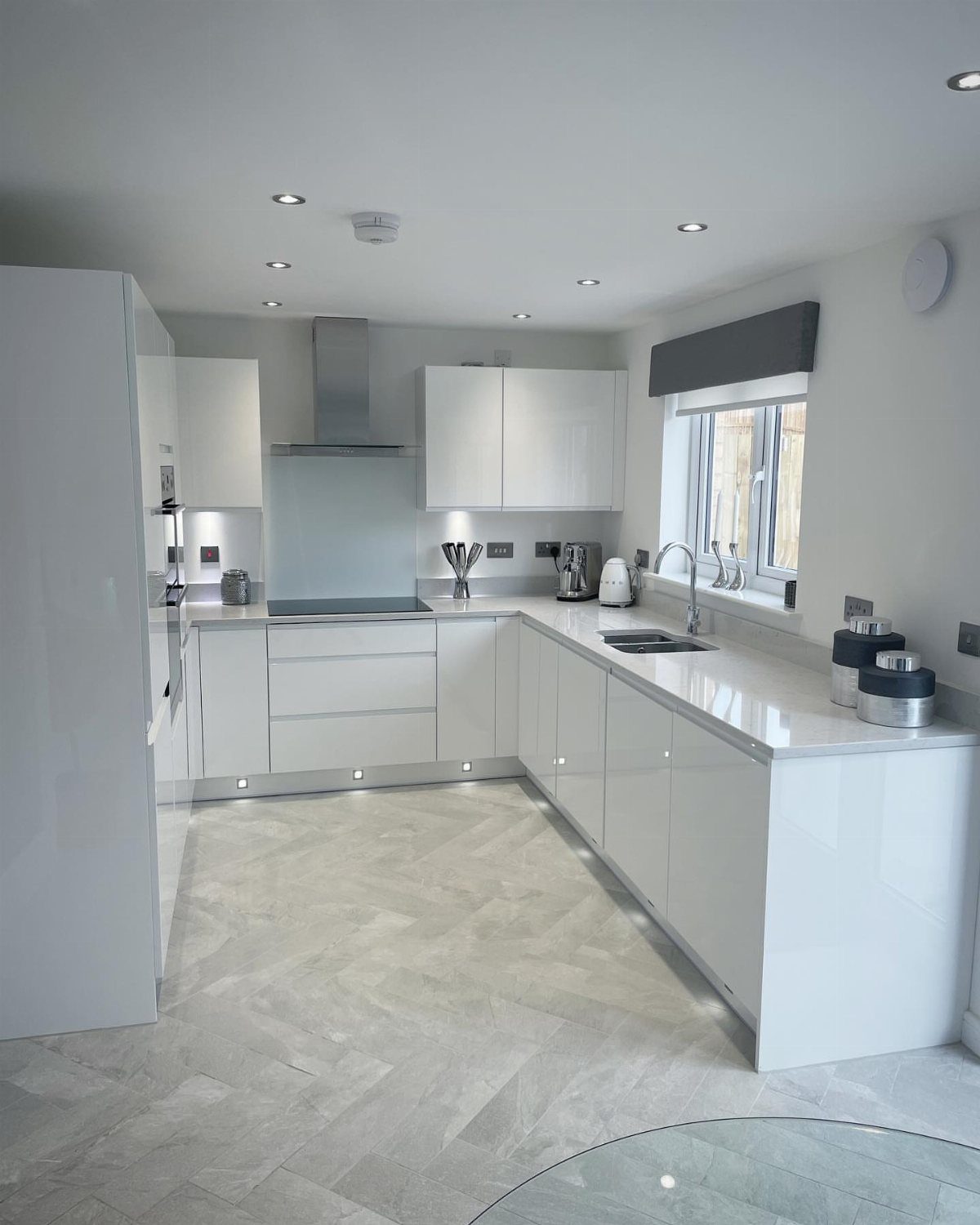 Off-white glossy kitchen cabinets illuminated by recessed ceiling and under-cabinet lighting.