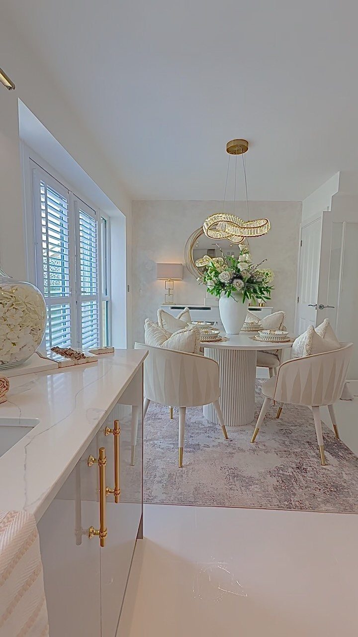 Off-white kitchen cabinets with gold hardware next to a luxurious white dining area.