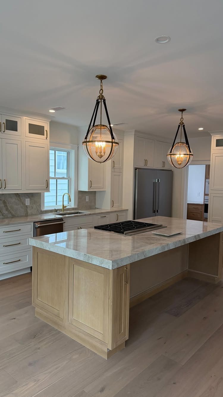 Off-white kitchen cabinets with a marble island and hanging orb pendant lights.