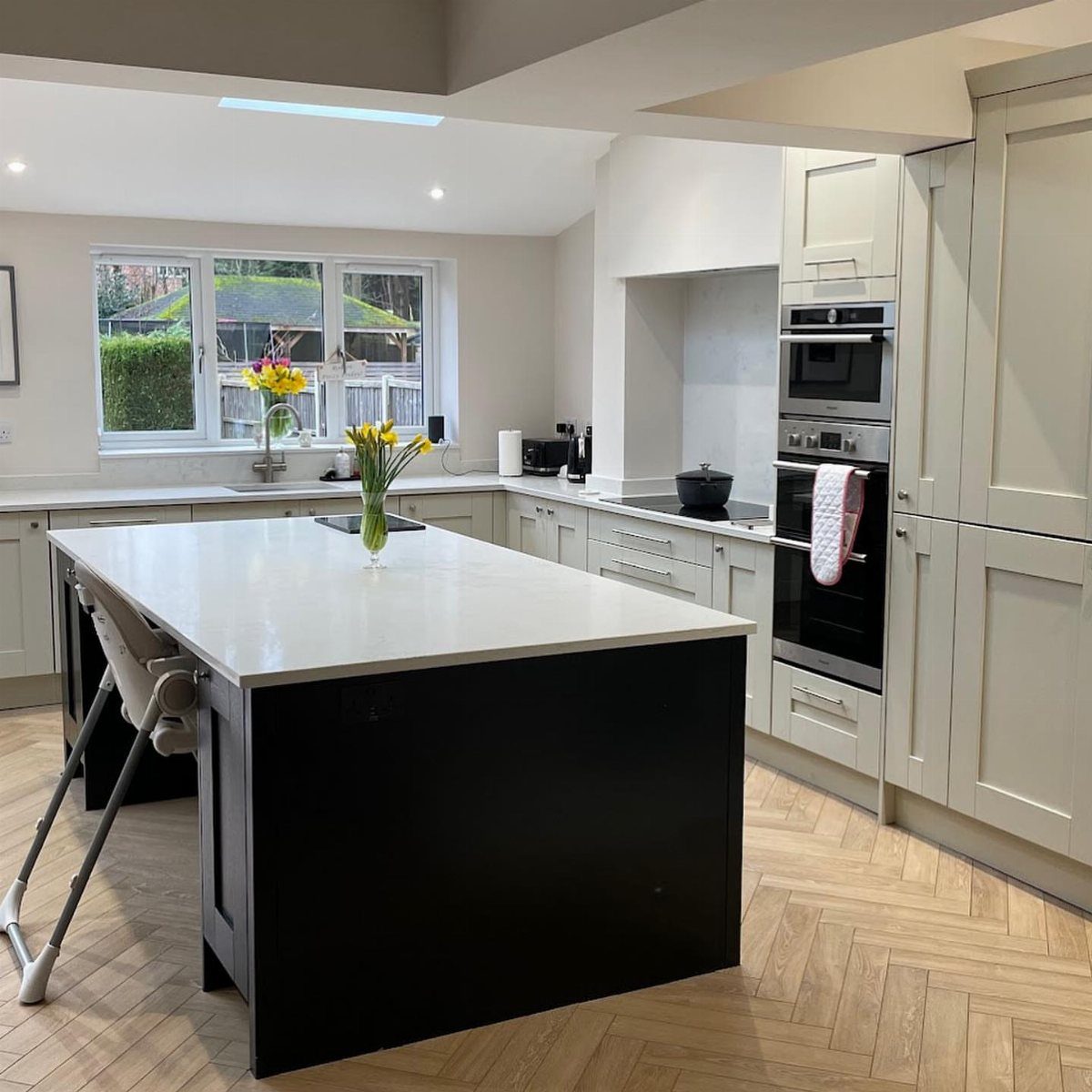 Off-white shaker kitchen cabinets with a black island and herringbone wood floors.