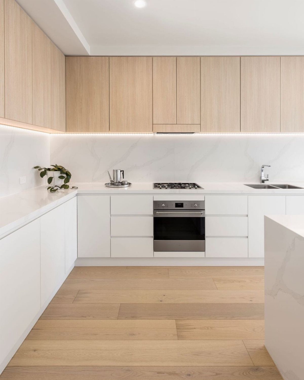 Off-white lower cabinets and light wood upper cabinets with white marble countertops.