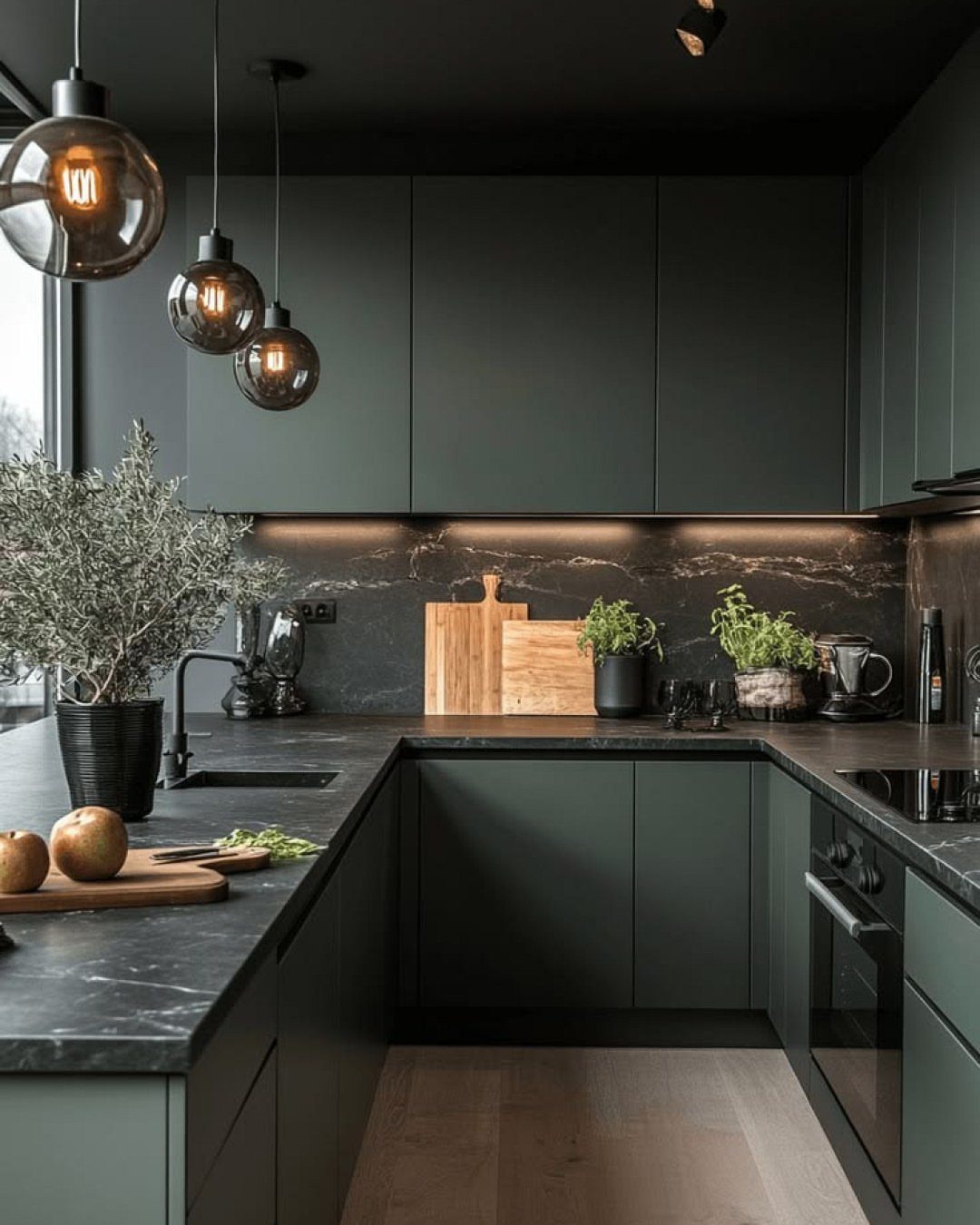 Dark olive green kitchen cabinets paired with black marble countertops and globe lighting.