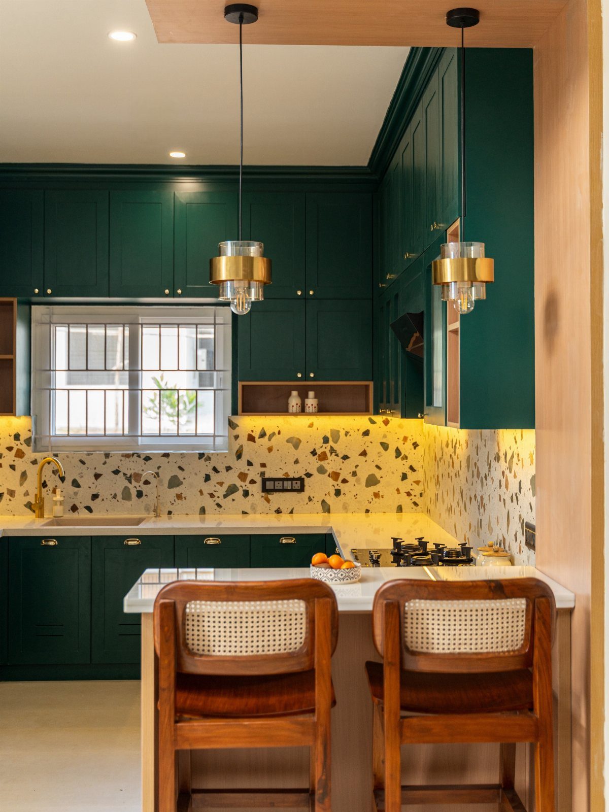 Dark olive green kitchen cabinets with wooden chairs and a light wood ceiling beam.