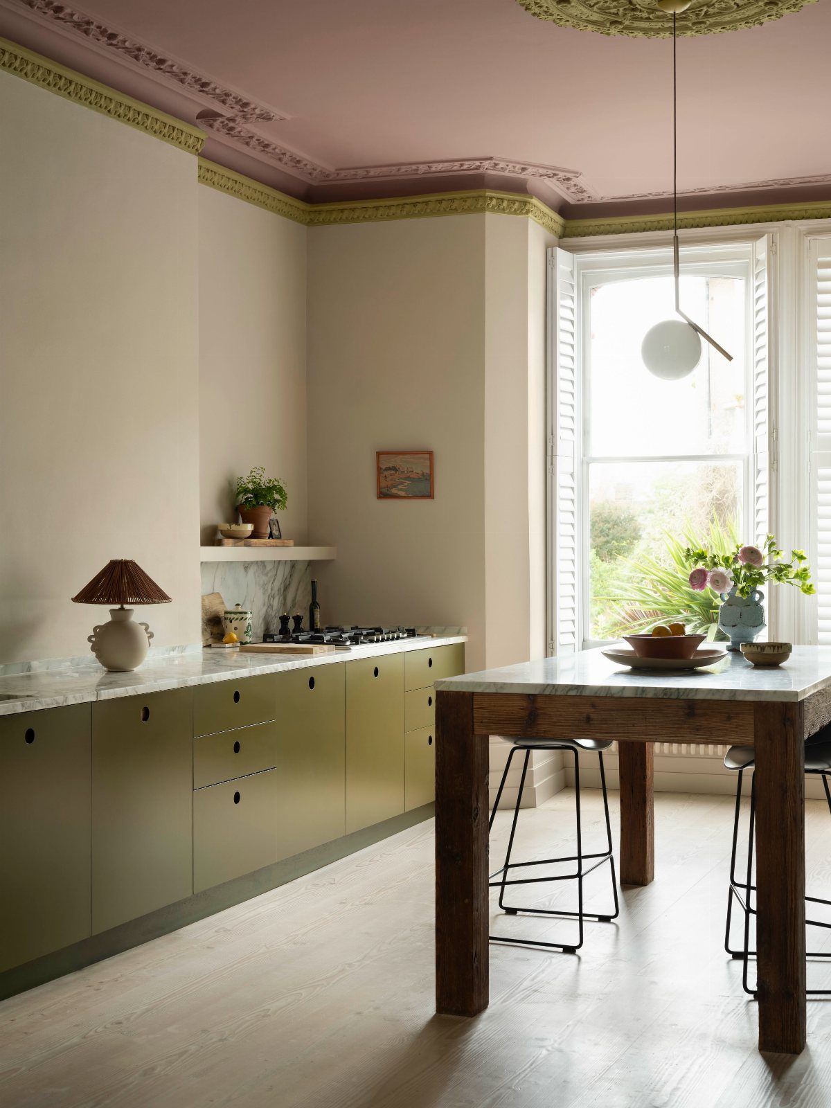 Olive green kitchen cabinets under a soft pink ceiling with gold crown molding.