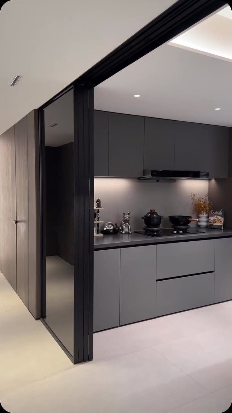Modern grey kitchen seen through a black-framed sliding glass door and partition.