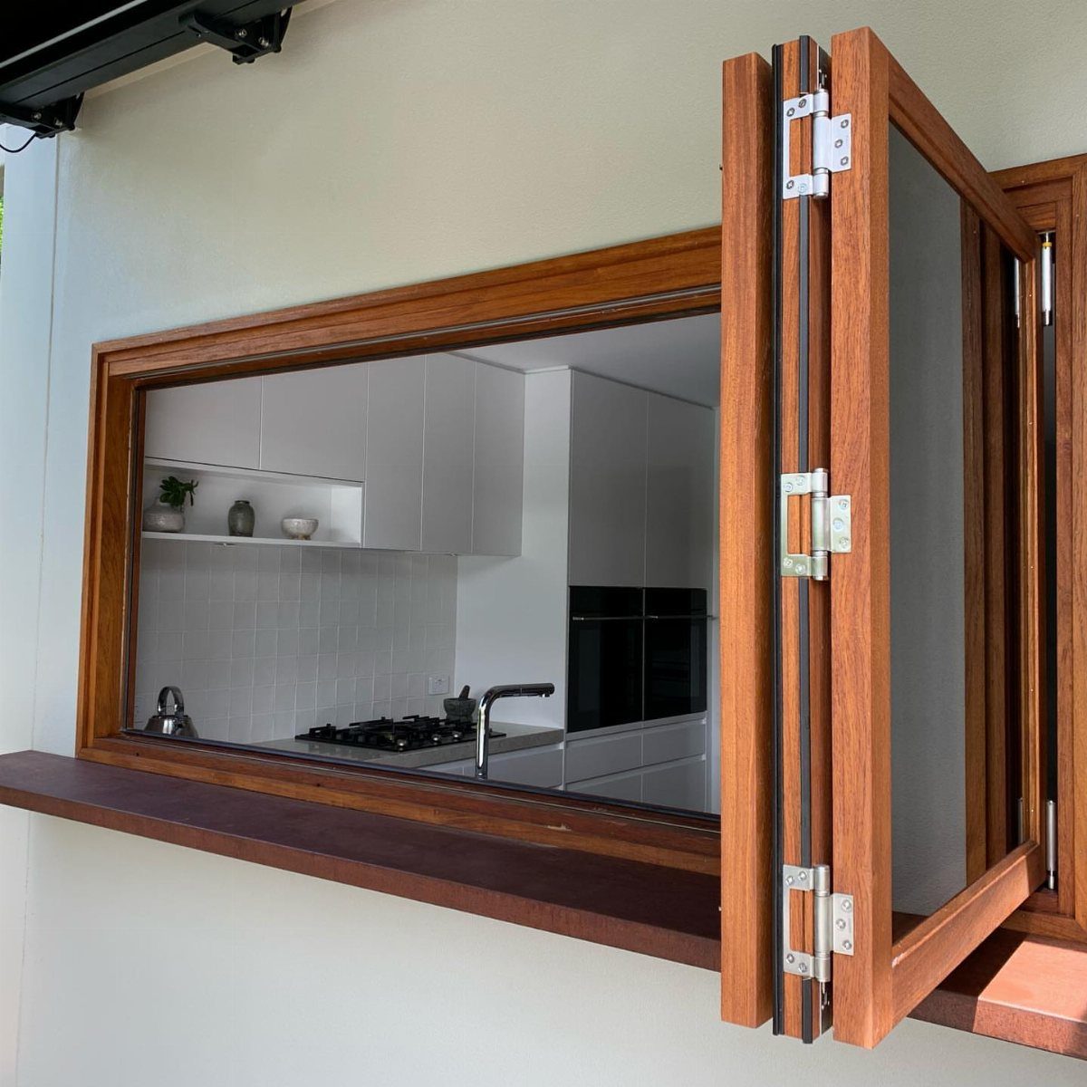 Wooden pass-through window opening into a modern white kitchen with a stovetop.