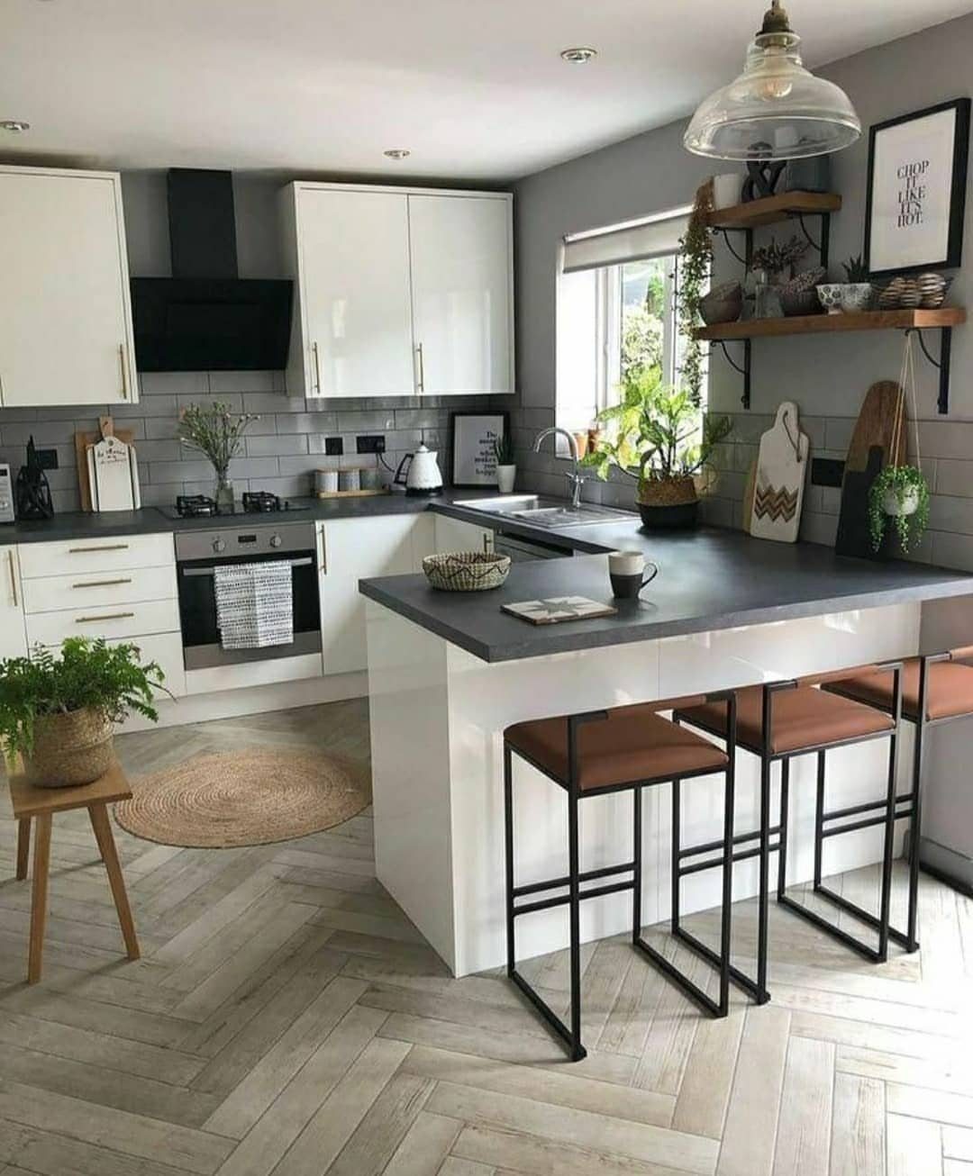 Kitchen peninsula with dark grey countertop and brown leather barstools on herringbone floors.