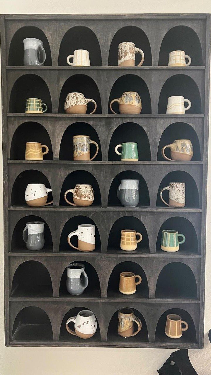 Dark grey arched wall shelving displaying a collection of colorful ceramic mugs.