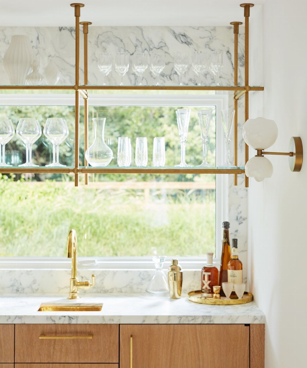 Glass shelves with gold frames holding glassware above a marble kitchen countertop
