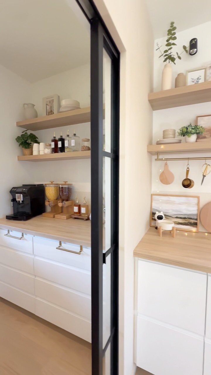 Light wood floating shelves above white kitchen cabinets with plants and jars.