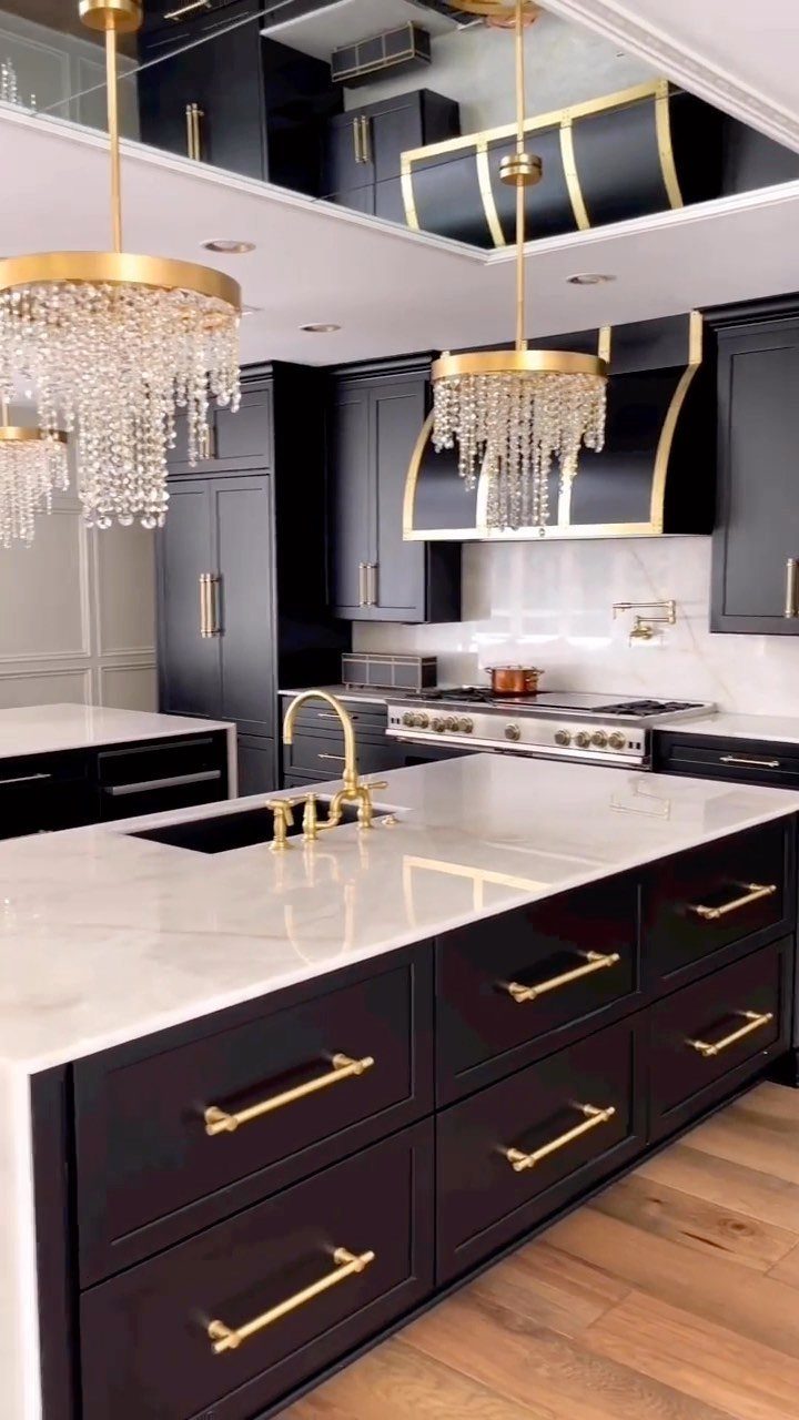 Black kitchen cabinets with gold hardware and white marble countertops under crystal chandeliers.