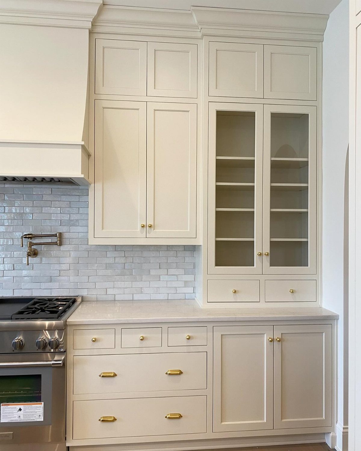 Cream kitchen cabinets with gold handles and a light gray tiled backsplash.