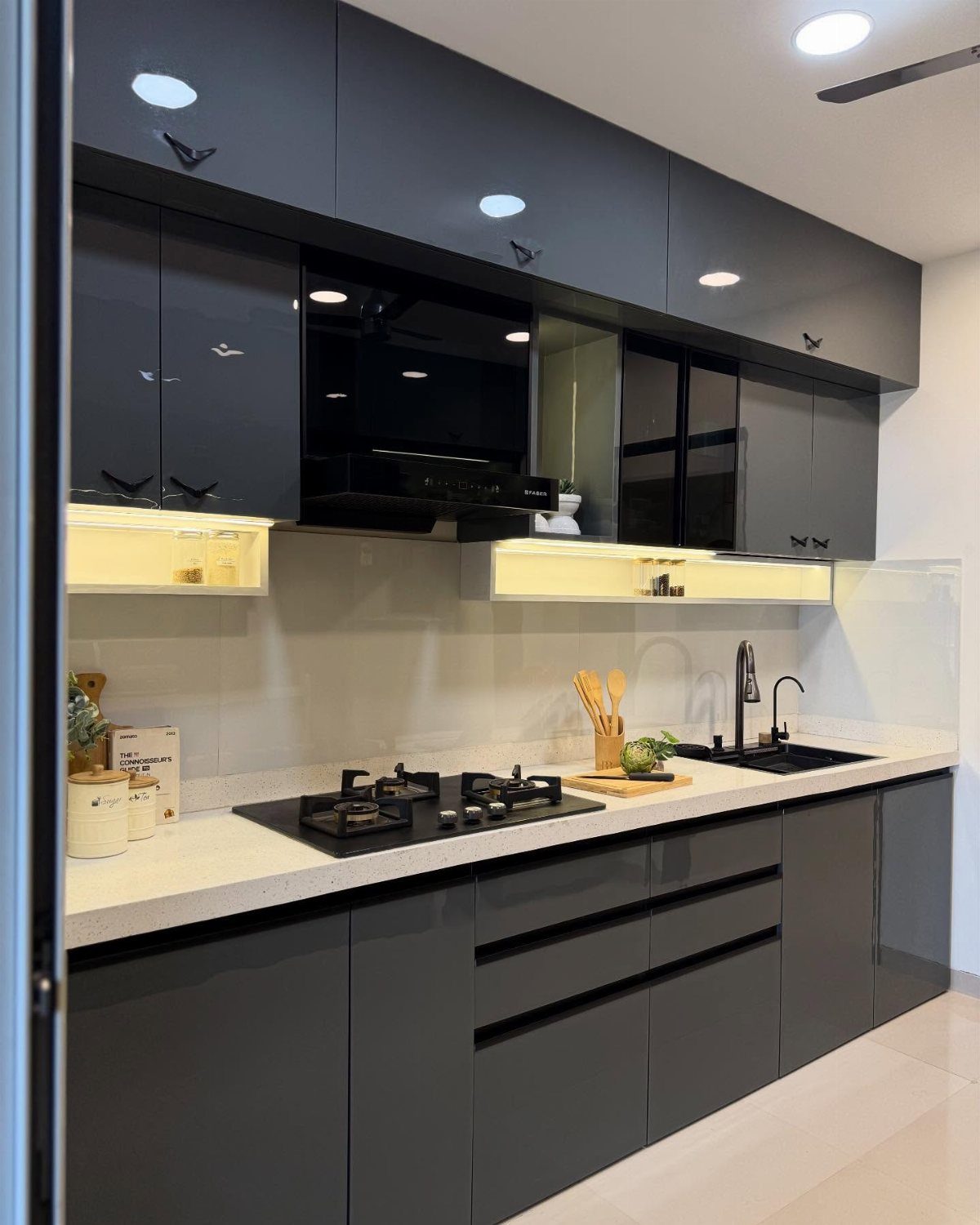 Dark gray glossy kitchen cabinets with white countertops and modern black appliances.