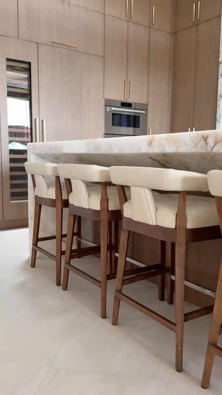 Light white oak kitchen cabinets with a marble island and cream bar stools.