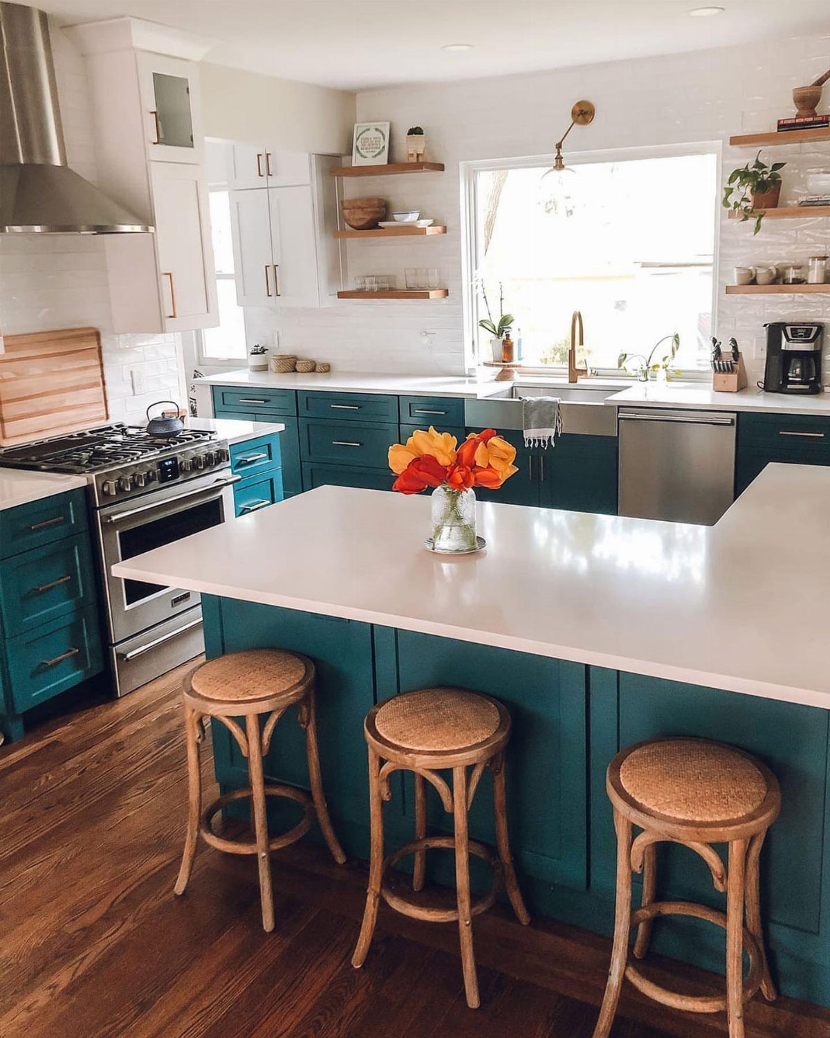 Teal kitchen cabinets and island with white countertops and woven wooden stools.