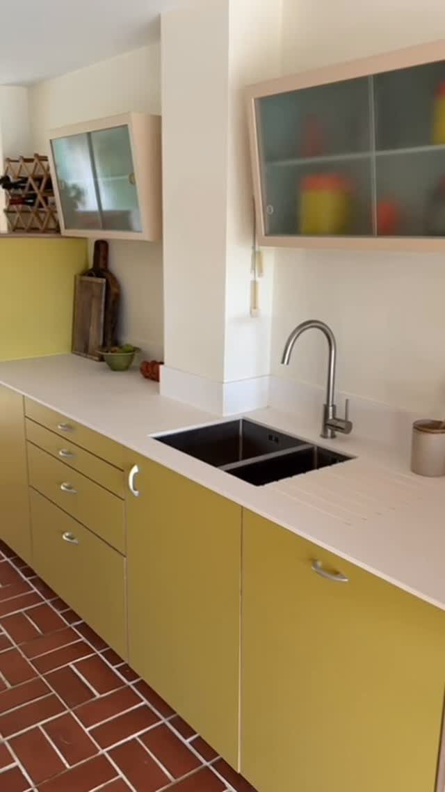 Butter yellow kitchen cabinets with white countertops and red brick tile flooring.